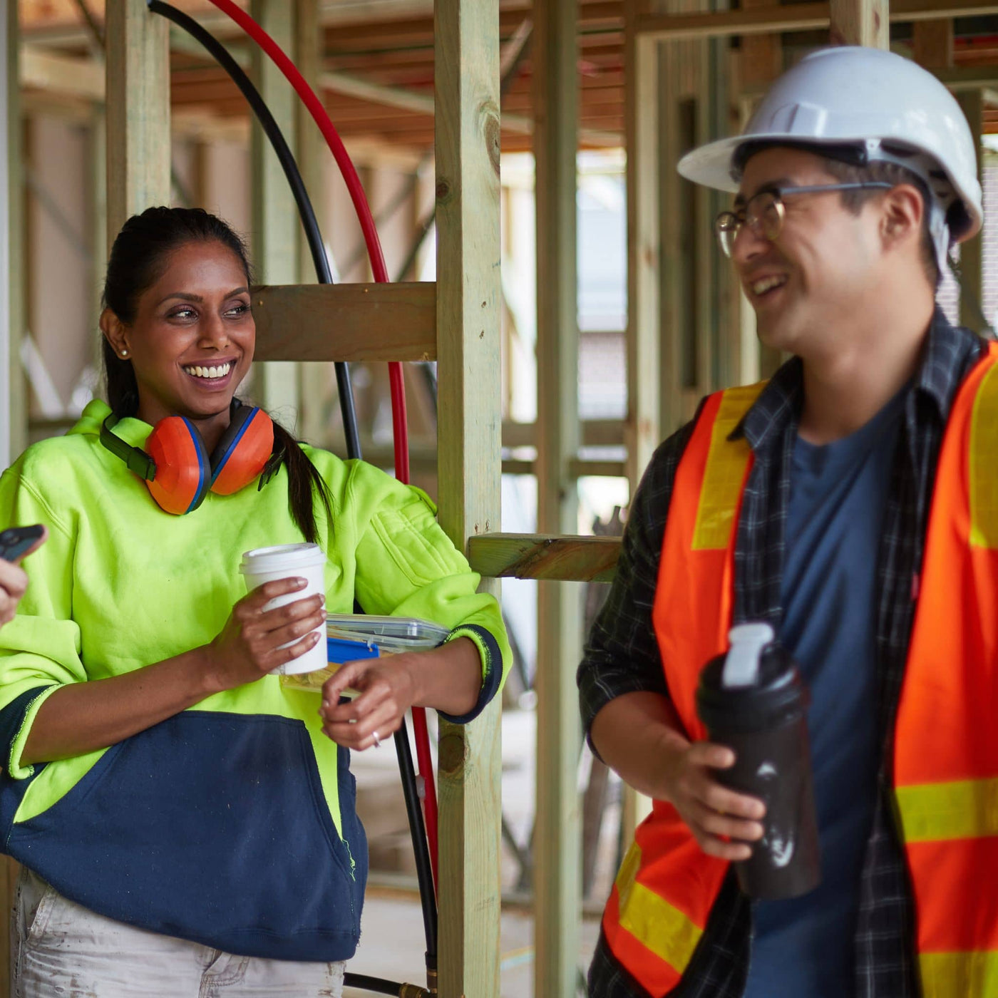 Two construction workers in a building under construction, one holding a coffee cup and the other a water bottle.